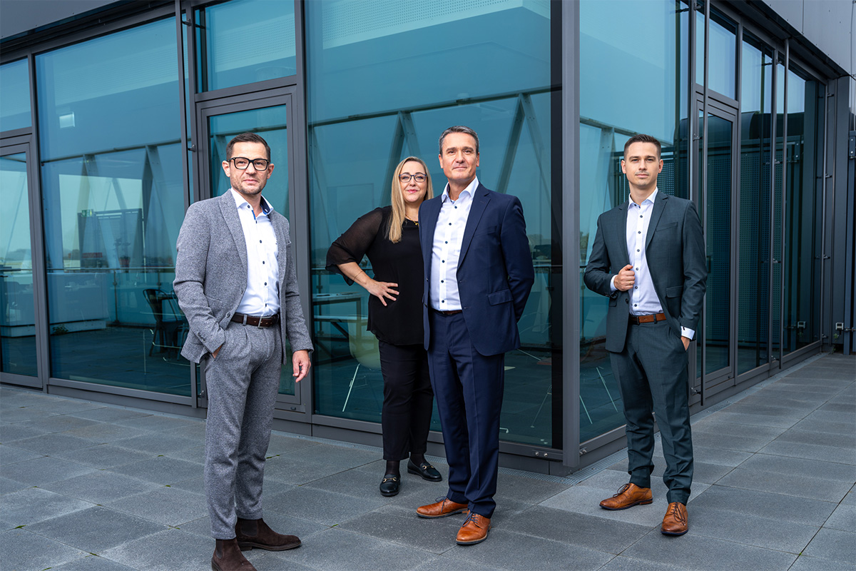 Vier professionell gekleidete Mitarbeiter von Azemos, einer banken- und produktunabhängigen Vermögensverwaltung mit Sitz in Offenburg, stehen vor einem modernen Glasgebäude.