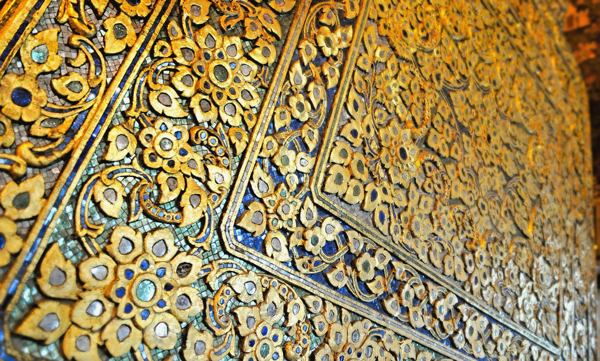 Ornate Wanddekoration mit goldenen Blumenmustern und blauen Akzenten, die durch detaillierte Mosaikarbeit und präzise Handwerkskunst besticht – ein Symbol für Wertigkeit und Tradition, passend zu Azemos’ Fokus auf reale Werte wie Gold.