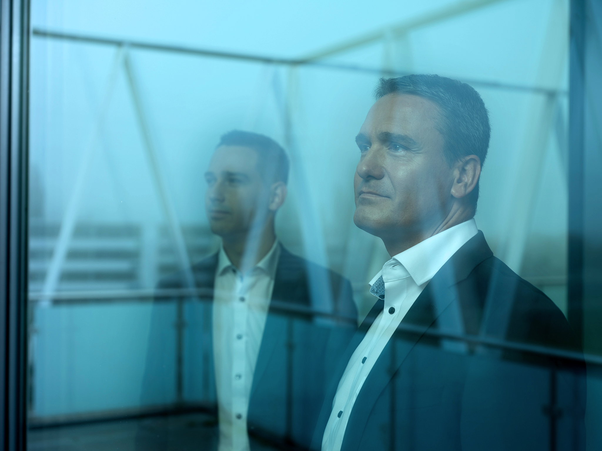 Ein professionell gekleideter Mann in Anzug steht vor einer Glaswand, sein Spiegelbild unterstreicht die seriöse, moderne Atmosphäre eines konservativen Vermögensverwalters wie Azemos, das auf langfristige, transparente Anlagestrategien fokussiert. Es handelt sich um den geschäftsführenden Gesellschafter Rainer Laborenz.