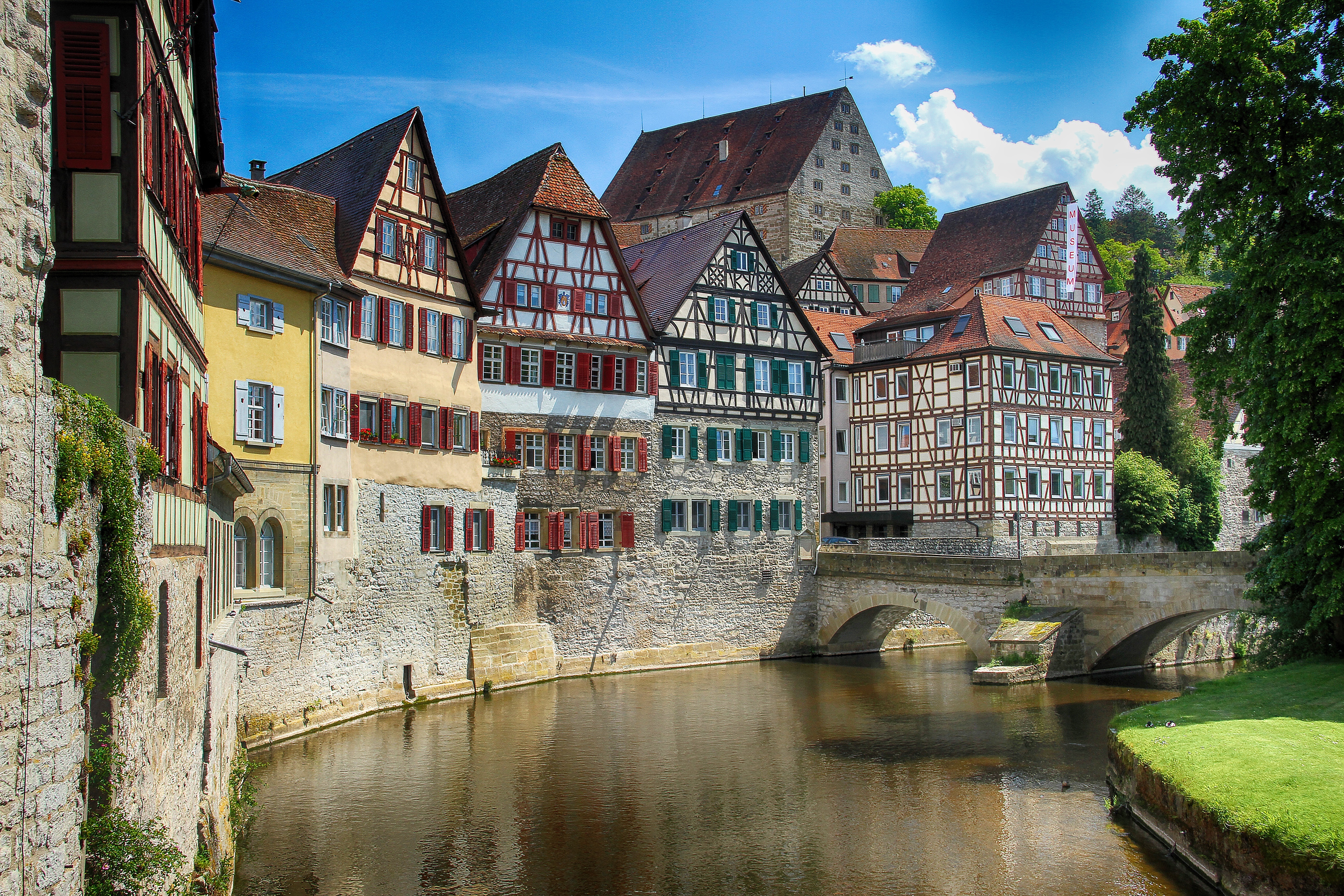 Idyllische Altstadt mit historischen Fachwerkhäusern, roten und grünen Fensterläden, Steinbrücke über einem Fluss und sonnigem Himmel, typisch für deutsche Städte wie Offenburg.